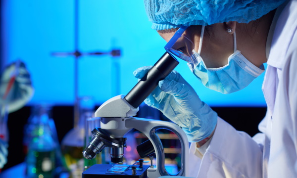 научные иследования Profile view of concentrated Asian microbiologist examining sample with help of modern microscope while wrapped up in work at dim laboratory